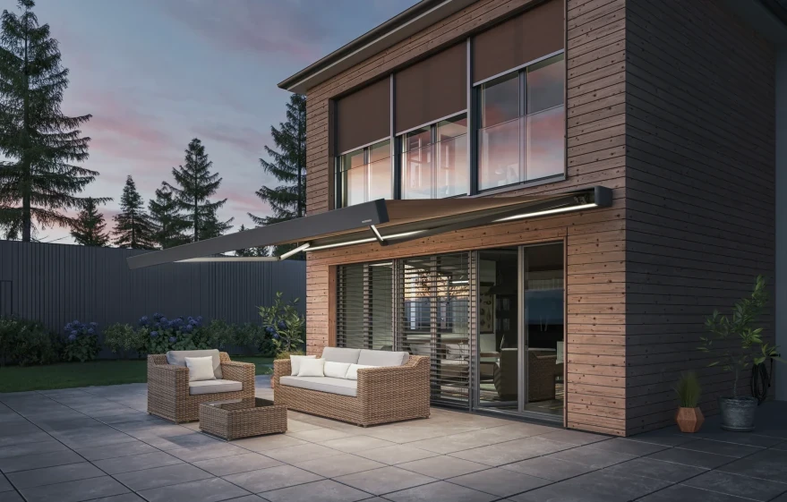 Moderne Holzfassade mit Markise über Terrasse und Loungemöbeln am Abend